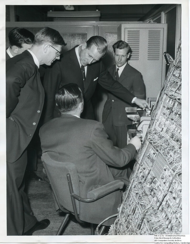 Prince Philip asking a question about the operation of the LEO III wiring plane and paper tape reader with John Pinkerton on his left at LEO's computer works and factory on Minerva Road in Acton, London 22 March 1960