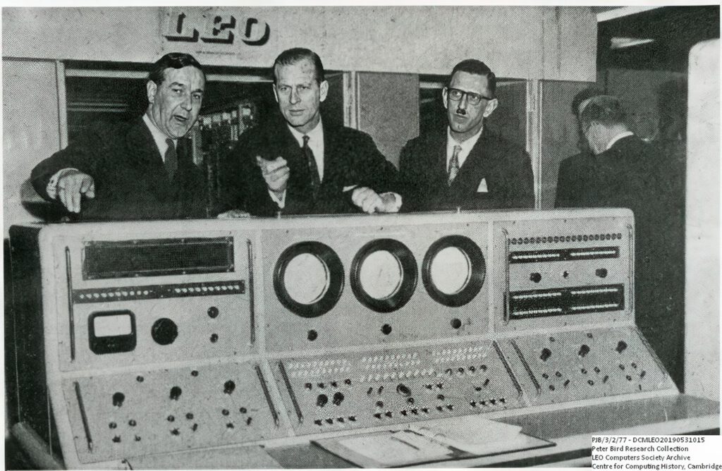 Photo of Prince Phillip (middle), Tony Barnes (left) and Anthony Salmon (right) behind a LEO computer at LEO's computer works and factory on Minerva Road in Acton, London 22 March 1960